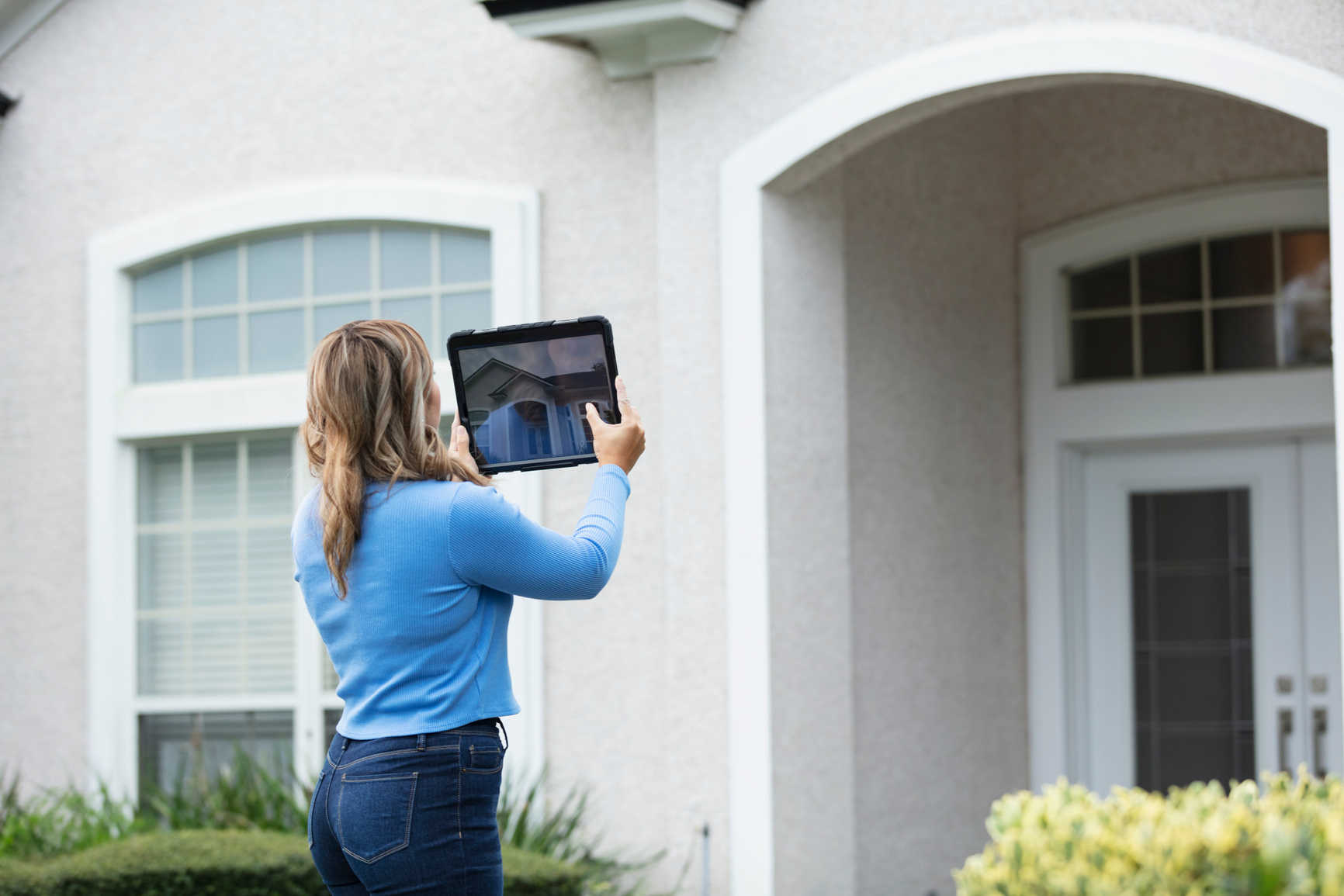 Female home appraiser photographs house with tablet